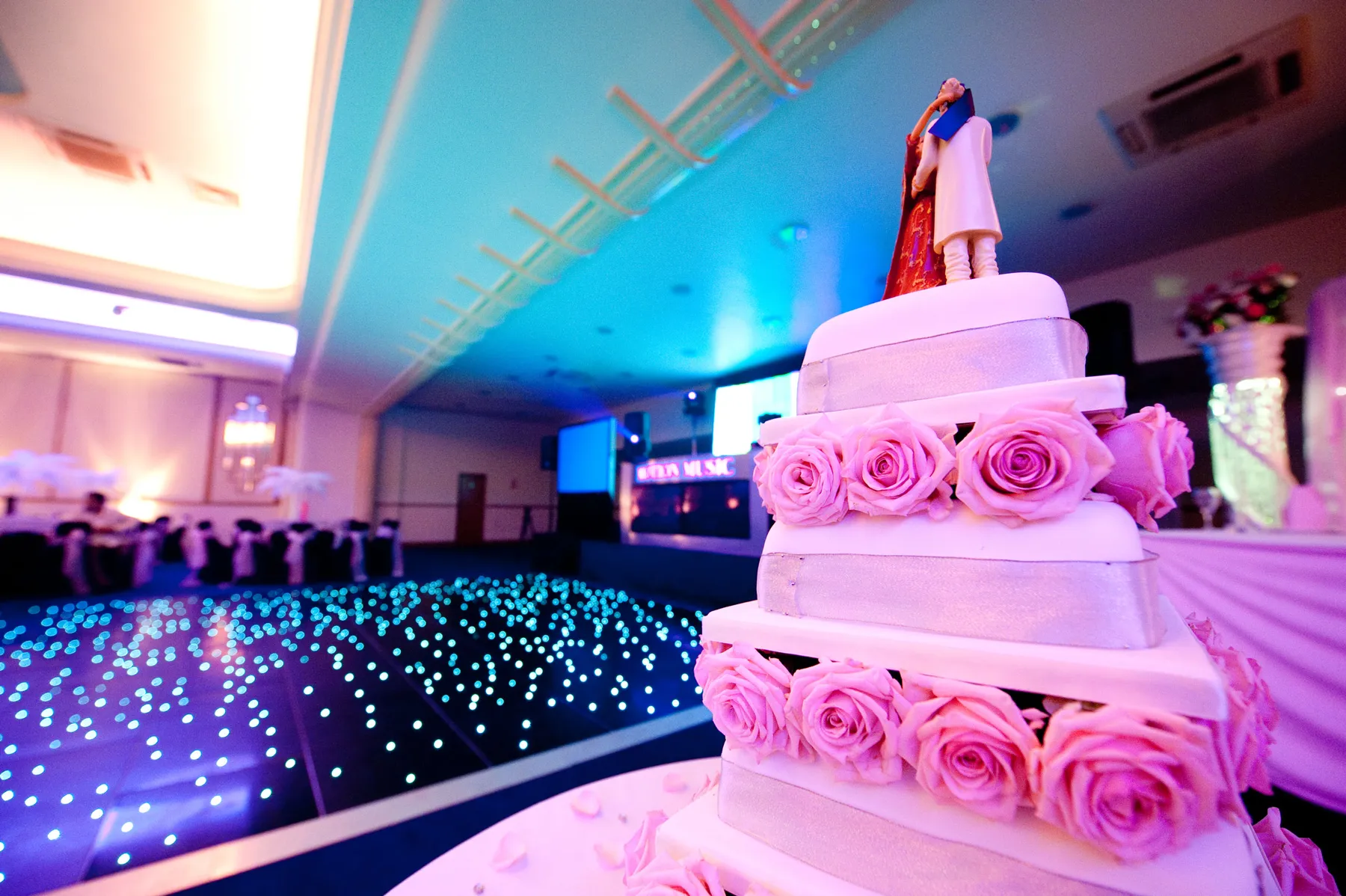 A wedding cake with pink roses on a starlit dance floor