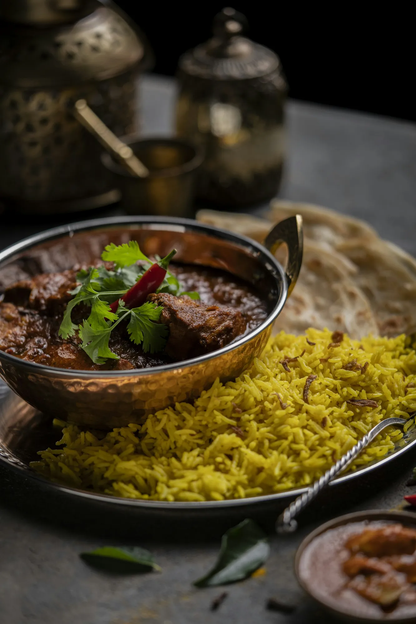 A curry in a copper bowl with yellow rice and naan